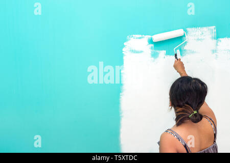 Young unidentifiable Asian woman painting wall with paint roller and copy space for text Stock Photo