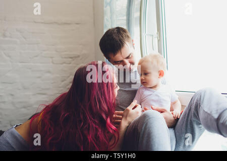 happy family of mother, father and child son playing and cuddling at home on floor near a big window. Stock Photo
