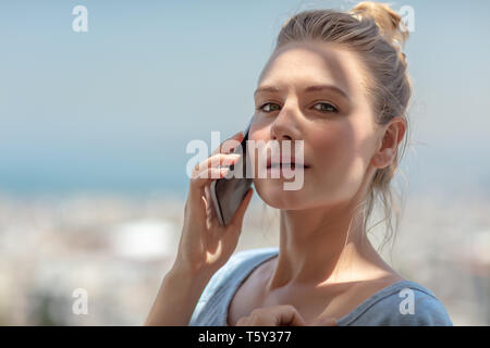 Portrait of a pretty female with pleasure speaking on the phone outdoors, positive girl communicating with someone on mobile, every day using technolo Stock Photo