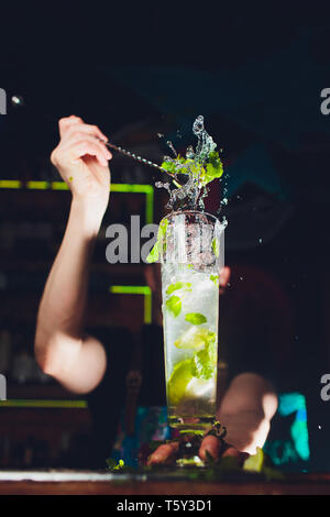 Mojito cocktail at the bar. Bartender preparing Mojito. Barman making cocktail with a lot of ice and lime at the bar. Mojito drink on black background Stock Photo