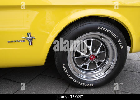 The wheel and badge on a yellow 1965 Ford Mustang 4700cc car at a classic motor vehicle show in the UK. American automobile. Stock Photo