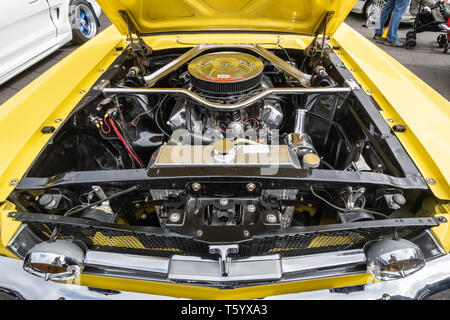 Close-up of the engine of a yellow 1965 Ford Mustang 4700cc car at a classic motor vehicle show in the UK. American automobile with hood open. Stock Photo