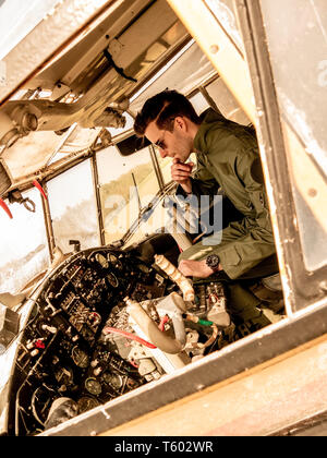 A handsome young man pilot in a green overall sitting in the cockpit of an old plane on a sunny day. Stock Photo