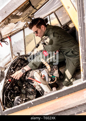 A handsome young man pilot in a green overall sitting in the cockpit of an old plane on a sunny day. Stock Photo