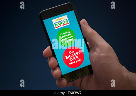 A man looks at his iPhone which displays the People's Postcode Lottery logo (Editorial use only). Stock Photo