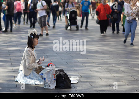 Asian lady sitting with a teddy bear on her head begging in London Stock Photo