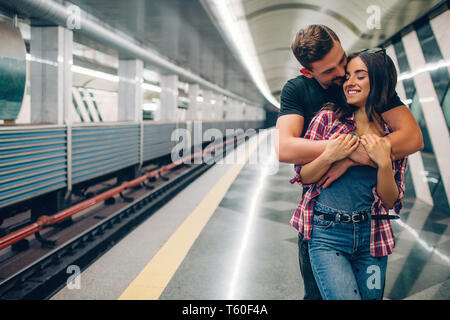 Young man and woman use underground. Couple in subway. He stand behind her and embrace. Kissing scene. Cheerful young woman smile. Love story Stock Photo