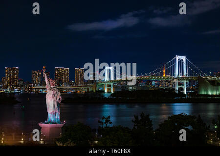 Odaiba's Rainbow Bridge and Tokyo Tower seen in the distant against night sky and Statue of Liberty in the foreground Stock Photo