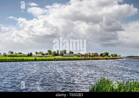 De Donk hamlet built on a low river dune  at the banks of a canal in the Alblasserwaard polder in the Netherlands under a cloudy sky in springtime Stock Photo