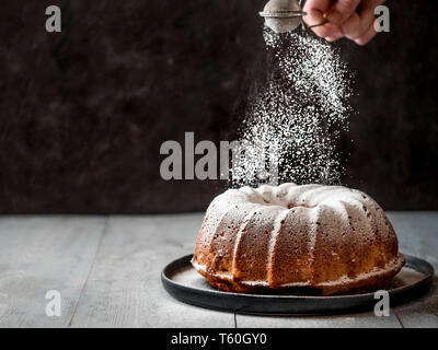 Woman's hand sprinkling icing sugar over fresh muffin cake. Powder sugar falls on fresh perfect muffin cake. Copy space for text. Ideas and recipes for breakfast or dessert Stock Photo