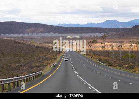 long stretch of tarred or asphalt road in the dry and arid semi desert region of the Karoo in South Africa with a solar energy farm up ahead Stock Photo