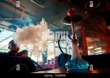 a man smokes a hookah sitting on a chair in a dark room Stock Photo