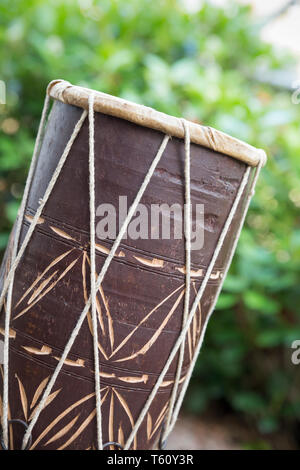 Close-up side view of a simple, traditional African hand drum (musical percussion instrument) in outdoor, natural setting. Stock Photo