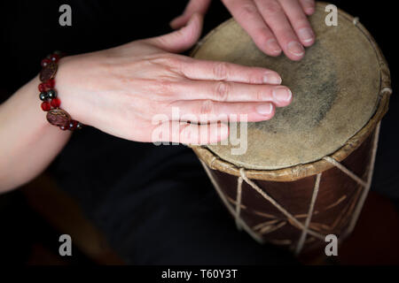 Close up of female hands playing simple, traditional African hand drum (tapping rhythm with finger tips) both hands resting on natural skin drum head. Stock Photo
