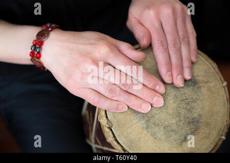Close up of female hands playing simple, traditional African hand drum (tapping rhythm with finger tips) both hands resting on natural skin drum head. Stock Photo