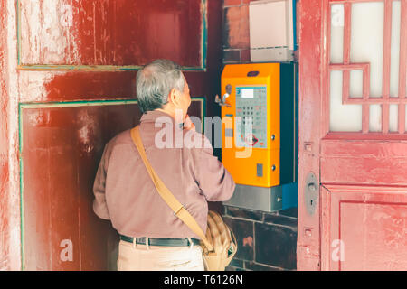 Old Taiwanese man (elderly man) using a payphone to call his relative at Longshan Temple in Wanhua district of Taipei, Taiwan Stock Photo