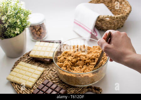 A Woman Making 3 Chocolates cake Pie, Ingredients on the table. Kitchen with white, dark and milk chocolate. Hazelnuts jar. Biscuits dough Stock Photo