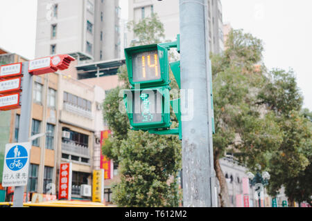 Pedestrian Traffic light in Taiwan showing green light and timer with old building and local business in the background Stock Photo