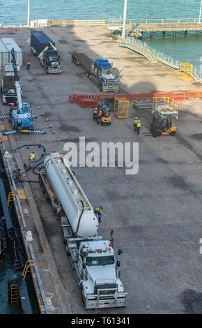 Darwin Australia - February 22, 2019: Gray tanker truck parked along ship is refueling the vessel. Other trucks and people on the dock. Stock Photo