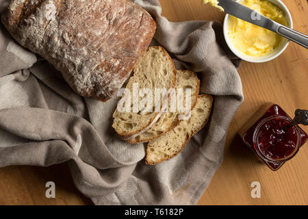 Sourdough bread and slices with butter and knife on kitchen cloth - Overhead image Stock Photo