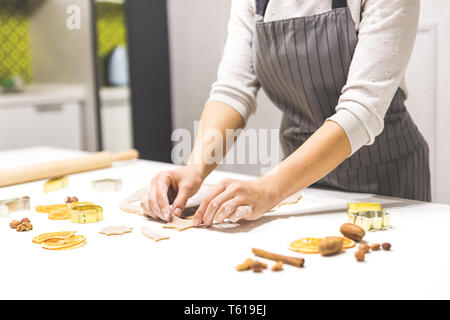 Young pretty woman prepares the dough and bakes gingerbread and cookies in the kitchen. She makes a star shape on the dough. Merry Christmas and Happy Stock Photo