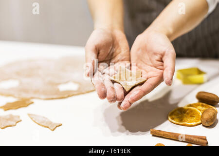 Young pretty woman prepares the dough and bakes gingerbread and cookies in the kitchen. She holds a star cut from the dough in her hands. Merry Stock Photo