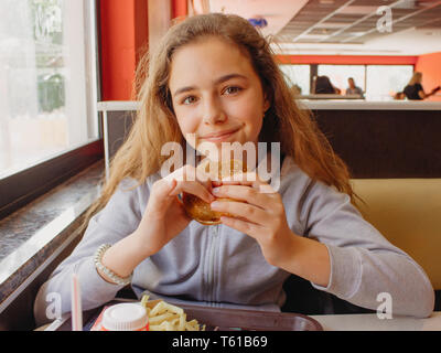 Pretty young teen girl with an appetite eating hamburger in a cafe Stock Photo