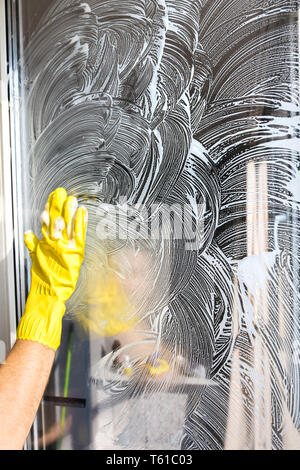 Close-up of a woman in uniform and yellow gloves washes a windows with window scraper. Professional home cleaning Stock Photo
