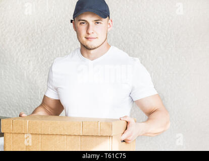 Delivery strong, muscular man loading cardboard boxes for moving to an apartment. professional worker of transportation, male loaders in overalls Stock Photo