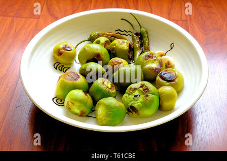 Roasted green tomatillos and serrano peppers in a decorative platter; some of the ingredients for green salsa or salsa verde. Stock Photo