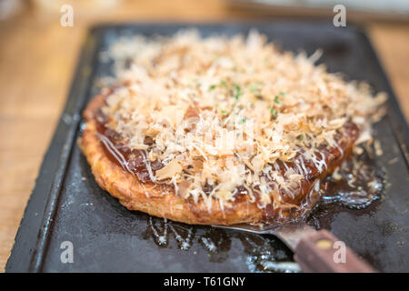 okonomiyaki; tranditional Japanese food style handmade and cut on a iron plate ready to serve and eat at a restaurant. close up shot. Stock Photo