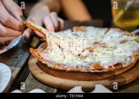 Woman's hand take pizza pices out from pizza plate in foodtruck event, Cheese's pizza is stretced by her. Stock Photo