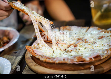 Woman's hand take pizza pices out from pizza plate in foodtruck event, Cheese's pizza is stretced by her. Stock Photo