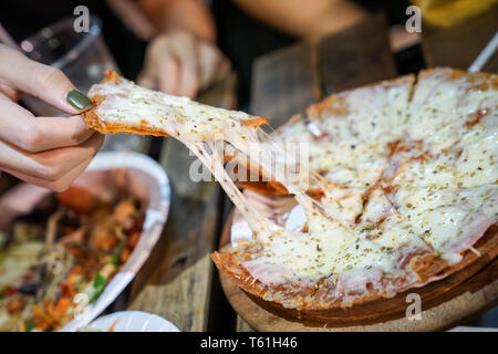 Woman's hand take pizza pices out from pizza plate in foodtruck event, Cheese's pizza is stretced by her. Stock Photo