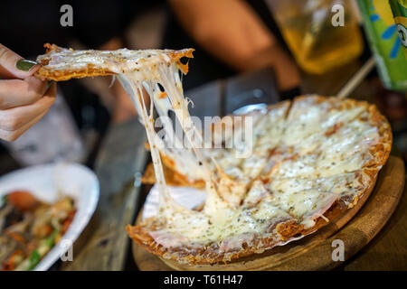 Woman's hand take pizza pices out from pizza plate in foodtruck event, Cheese's pizza is stretced by her. Stock Photo