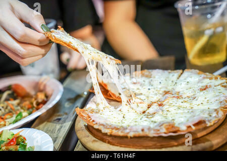 Woman's hand take pizza pices out from pizza plate in foodtruck event, Cheese's pizza is stretced by her. Stock Photo