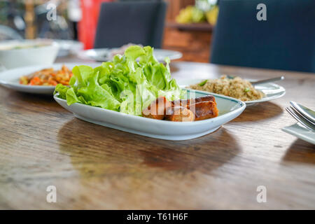 Sliced Notrhern Thai Spicy Sausage 'Sai Aua' on white tile disk, decorate by green oak. Stock Photo