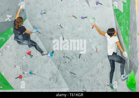 Rock climber woman hanging on a bouldering climbing wall, inside on colored hooks Stock Photo