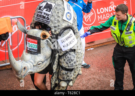 London, UK. 28th Apil 2019. Rhino Harry, running for 'Save the Rhino', is helped at the finish line. Over 40,000 starters are once again competing in the Virgin London Marathon, including those who take on the race for charities, in running clubs, in memory of loved ones and as personal lifetime goals. Credit: Imageplotter/Alamy Live News Stock Photo