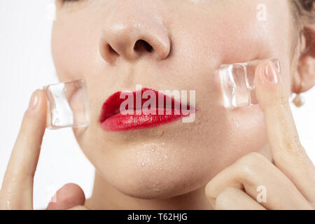 serious young woman applying ice cubes on her face skin, isolated on white background Stock Photo