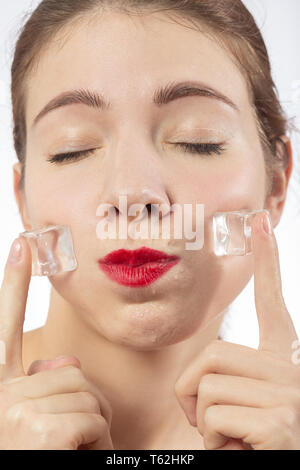 serious young woman applying ice cubes on her face skin, isolated on white background Stock Photo