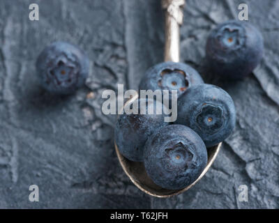 Freshly picked blueberries in spoon closeup. Ripe and juicy fresh blueberries on textured concrete background. Bilberry on dark background with copyspace. Blueberry antioxidant. Healthy eating concept Stock Photo