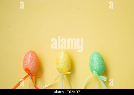 Three colorful Easter eggs on pale yellow background, colorful eggs decor, green, orange, yellow, egg hunt decoration, flat lay with copy space for te Stock Photo