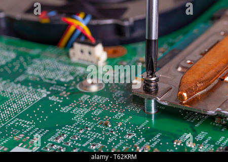 A screwdriver unscrews the mounting bolt of the computer board Disassembly, repair and cleaning of electronics. Part of laptop Stock Photo