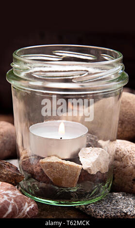 upright white burning tea light candle glass stones center dark background  by jziprian Stock Photo