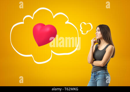 Young thinking brunette girl wearing casual jeans and t-shirt with red heart on yellow background Stock Photo