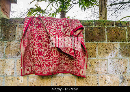 Red traditional persian carpet hanging outside over a stone wall Stock Photo