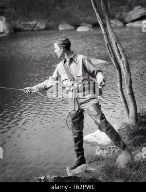 1920s 1930s YOUNG MIDDLE AGE MAN SPORTSMAN FLY FISHING FROM SPRINGTIME RIVER BANK BUT WEARING RUBBER WADERS - a2786 HAR001 HARS COPY SPACE FULL-LENGTH PHYSICAL FITNESS PERSONS MALES HOOK SERENITY SPIRITUALITY CONFIDENCE B&W CATCHING FREEDOM SKILL ACTIVITY AMUSEMENT HAPPINESS PHYSICAL WELLNESS ADVENTURE HOBBY LEISURE STRENGTH STRATEGY INTEREST CHOICE HOBBIES KNOWLEDGE PASSION RECREATION PASTIME PRIDE REEL PLEASURE CONCEPTUAL BUT ESCAPE FLEXIBILITY MUSCLES STYLISH WADERS MIDDLE AGE SPORTSMAN MID-ADULT MID-ADULT MAN RELAXATION SPRINGTIME WILDLIFE AMATEUR BLACK AND WHITE CAUCASIAN ETHNICITY Stock Photo
