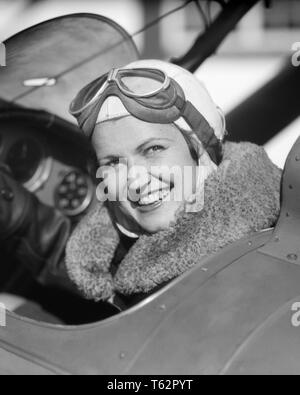 1930S woman pilot sitting in cockpit of airplane smiling looking at camera fur collar on jacket and goggles pushed up on head - a4370 HAR001 HARS FACIAL STYLE WELCOME PLEASED JOY LIFESTYLE PLANES FEMALES JOBS LADIES PERSONS GOGGLES RISK CONFIDENCE TRANSPORTATION EXPRESSIONS B&W EYE CONTACT SKILL OCCUPATION HAPPINESS SKILLS THRILL HEAD AND SHOULDERS CHEERFUL ADVENTURE AIRPLANES AND AT IN OF ON AVIATION EMPLOYMENT OCCUPATIONS PUSHED SMILES COCKPIT FUR COLLAR AVIATOR JOYFUL STYLISH AVIATRIX MID-ADULT MID-ADULT WOMAN BLACK AND WHITE BRAVE CAUCASIAN ETHNICITY HAR001 OLD FASHIONED Stock Photo