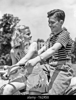 1930s 1940s SMILING TEENAGE BOY AND GIRL RIDING BICYCLE TOGETHER  - b1053 HAR001 HARS BALANCE PLEASED JOY LIFESTYLE FEMALES RURAL HEALTHINESS FRIENDSHIP HALF-LENGTH ADOLESCENT PERSONS CARING MALES TEENAGE GIRL TEENAGE BOY CONFIDENCE B&W HAPPINESS CHEERFUL RECREATION OPPORTUNITY SMILES CONNECTION JOYFUL STYLISH TEENAGED AFFECTION GROWTH JUVENILES MEETS TOGETHERNESS BLACK AND WHITE CAUCASIAN ETHNICITY HAR001 OLD FASHIONED Stock Photo